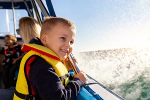 A young boy is wearing his life jacket when on the boat with his family