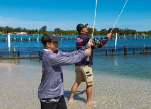 Father and son are casting their fishing rods into the lake form the shallows on a sunny day