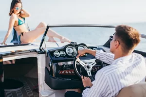 A guy is steering his new boat while his partner is catching some sun in her bikini on the front of the boat