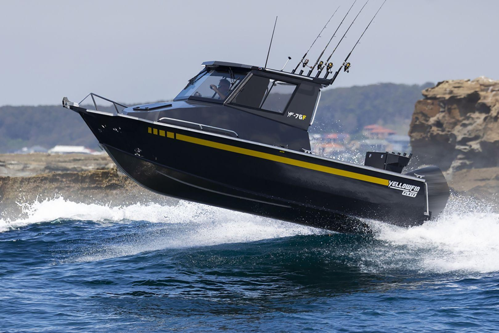 A YF-76 Extended Cabin boat jumping across swell in front of a rocky outcrop.