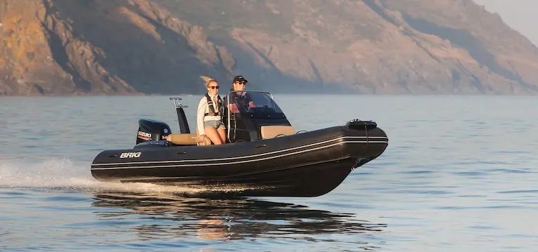 BRIG Eagle 6 RIB boat on water with two people, mountains in background.