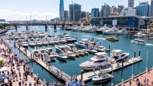 A couple browsing luxury motor cruisers moored at a sunny outdoor boat show marina.